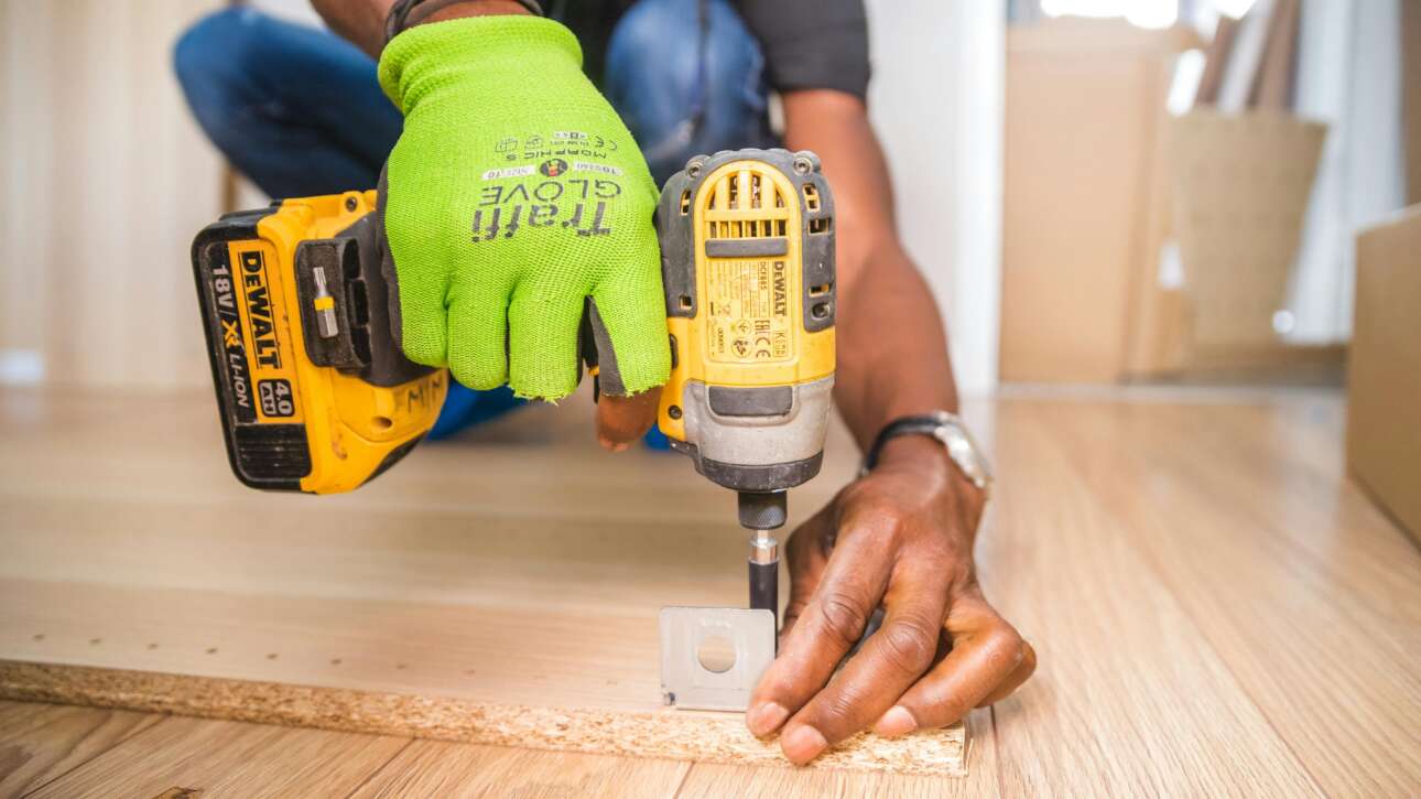Man using a power drill for home improvement on a wooden floor with precision.