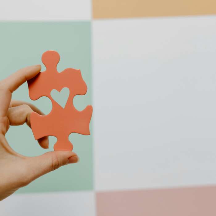 Close-up of a hand holding a heart-shaped puzzle piece against a colorful background.